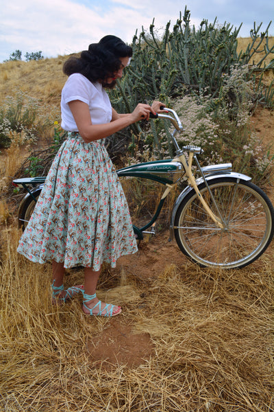 Model wearing the Lil' Lou Lou Jivin' Skirt in the Princess of the Forest woodland print while standing beside a vintage bicycle.