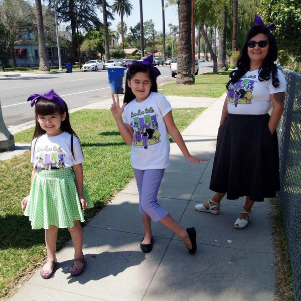 Mother and two daughters wearing matching Lou Lou Dolls Tees inspired by the diverse Lil' Lou Lou community and illustrated by Orange Dolly Cartoons.