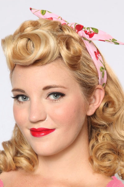 Woman wearing Pink Cherry Dots 4 in 1 headband with bow tied on top, featuring a pink background and red cherry print.