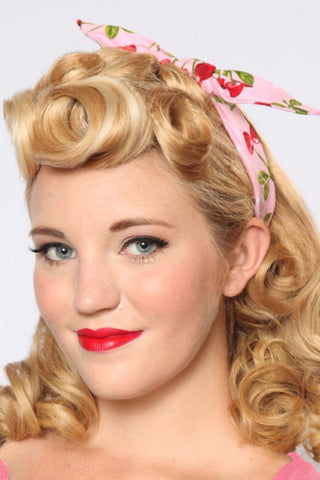Woman wearing Pink Cherry Dots 4 in 1 headband with bow tied on top, featuring a pink background and red cherry print.