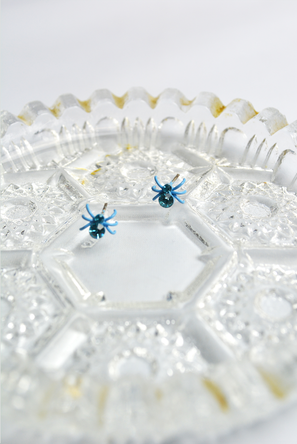 Baby blue crystal spider stud earrings with faceted crystal accents displayed on a vintage glass dish.