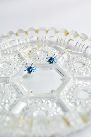 Baby blue crystal spider stud earrings with faceted crystal accents displayed on a vintage glass dish.