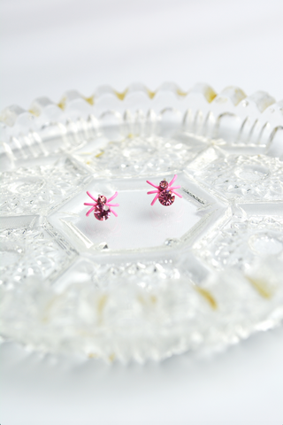 Pink Itsy Bitsy Spider earrings with faceted crystal accents and post-back closure on a decorative glass tray.