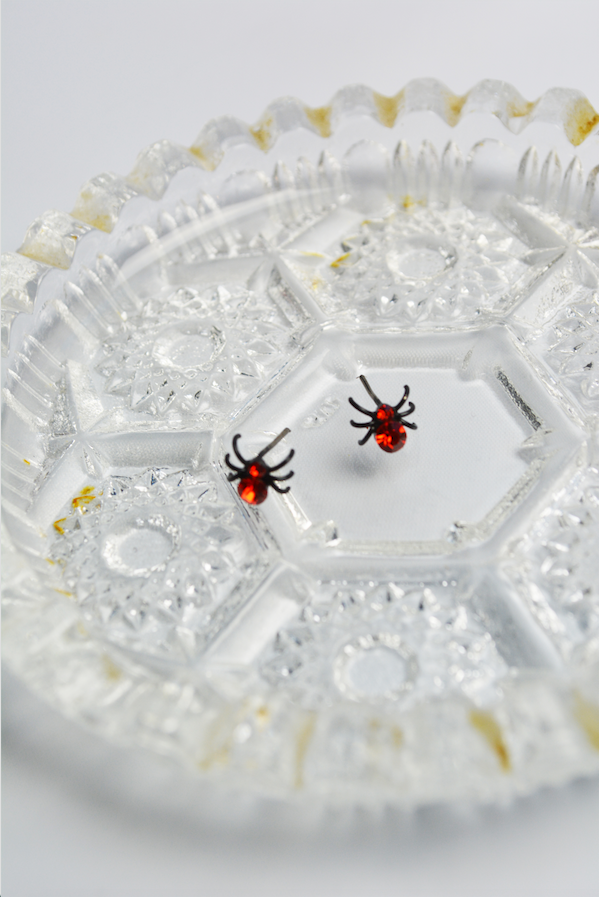 Red Itsy Bitsy Spider stud earrings with faceted crystal accents displayed on a vintage glass tray.