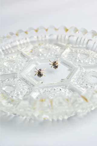 White Itsy Bitsy Spider stud earrings with faceted crystal accents displayed on a vintage glass tray.