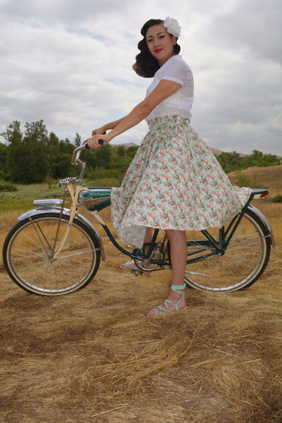 Model wearing the Lil' Lou Lou Jivin' Skirt in the Princess of the Forest woodland print, showcasing the full gathered silhouette beside a vintage bicycle.