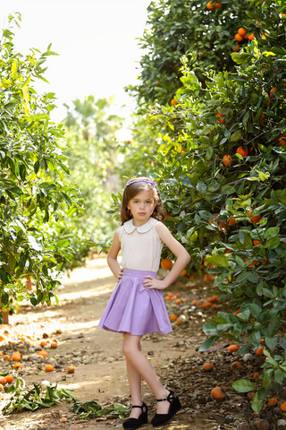 Girl wearing lilac Kids Jivin' Skirt by Lil' Lou Lou styled with Wendy Blouse and Jackie Headband in an outdoor orange grove.