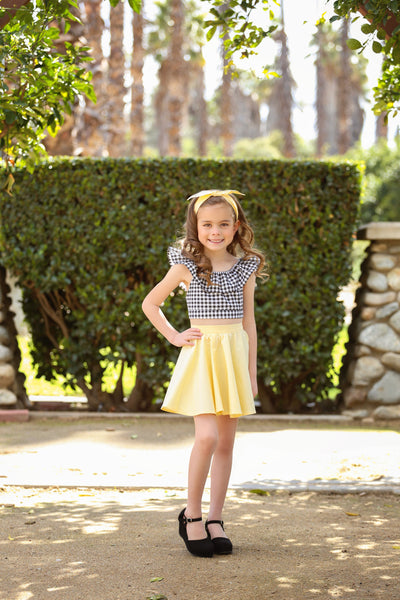 Girl wearing a yellow vintage inspired Kids Jivin' Skirt by Lil' Lou Lou with a gingham Cha Cha Top and matching bow headband.