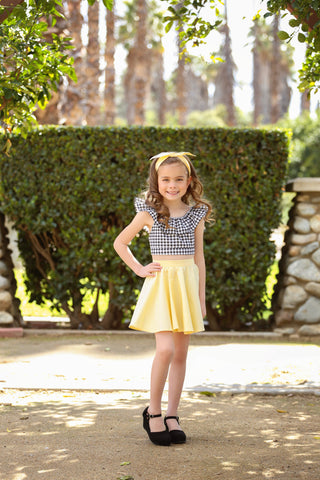 Girl wearing a yellow vintage inspired Kids Jivin' Skirt by Lil' Lou Lou with a gingham Cha Cha Top and matching bow headband.