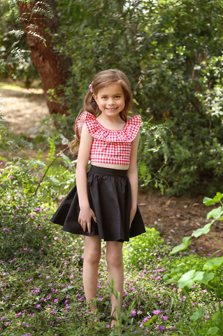 Girl wearing the Lil' Lou Lou Cha Cha Top in Red Picnic print paired with the Kids Jivin' Skirt and Cute Knotted Bow hair accessory.