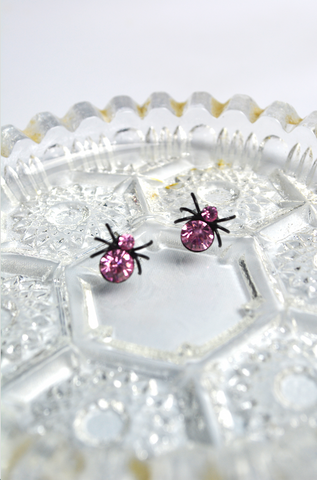 Pink House Spider stud earrings with faceted crystal accents displayed on a vintage crystal dish. Gothic spider earrings inspired by Lil' Lou Lou's Morticia's Garden collection.