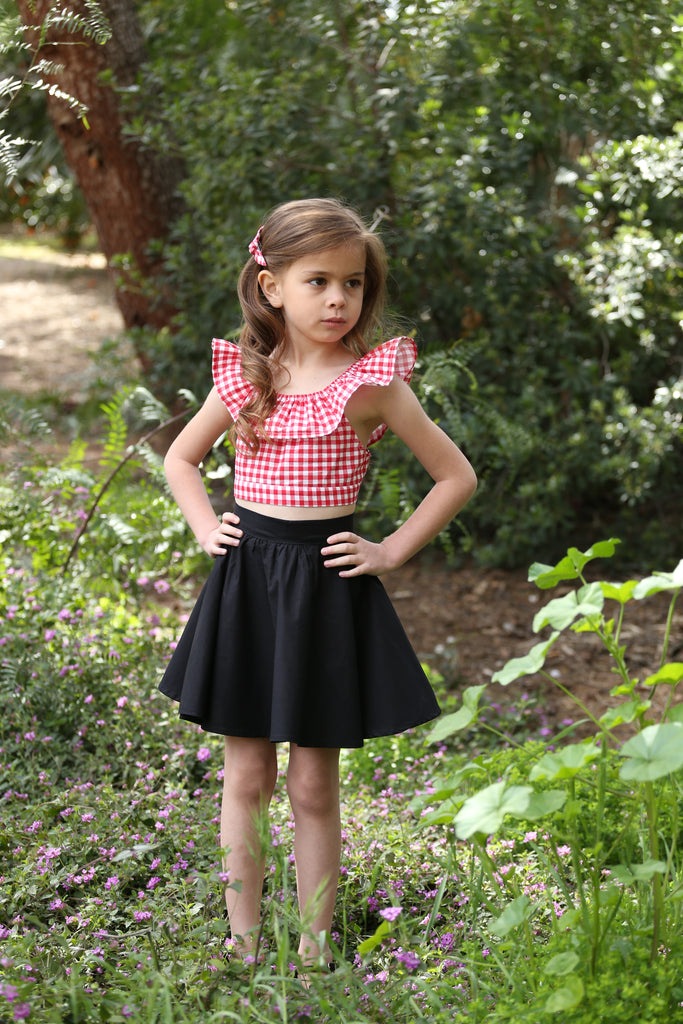 Girl wearing the Lil' Lou Lou Kids Jivin' Skirt in black with a Red Picnic gingham Cha Cha Top and matching hair accessory.