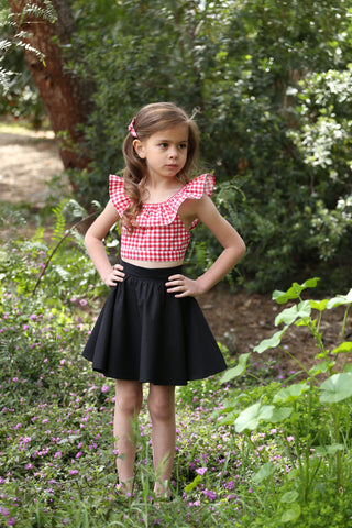Girl wearing the Lil' Lou Lou Kids Jivin' Skirt in black with a Red Picnic gingham Cha Cha Top and matching hair accessory.