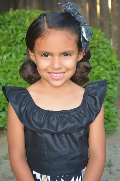 Girl wearing Lil' Lou Lou Cha Cha black ruffle crop top styled with a high waisted skirt, inspired by 1950s children's separates.