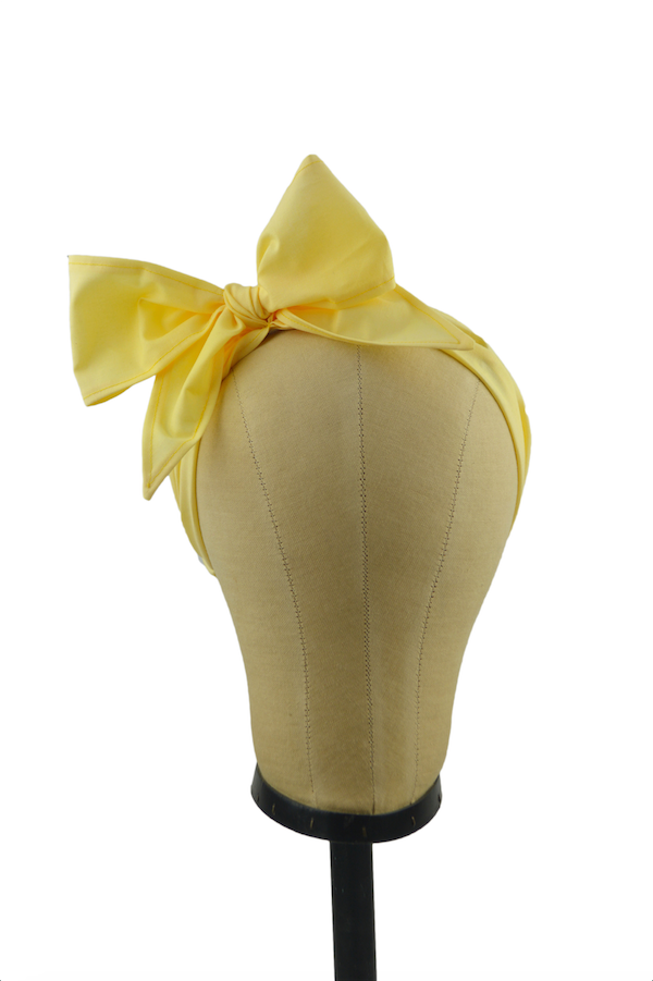 Front view of a yellow Minnie Headband with oversized bow displayed on a mannequin head, vintage-inspired cotton hair scarf headband by Lil' Lou Lou.