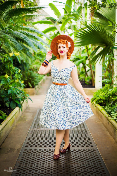 Model wearing the Lil' Lou Lou Razzle Dazzle Dress in ivory and navy woodland print styled with a hat and belt in a botanical garden setting.