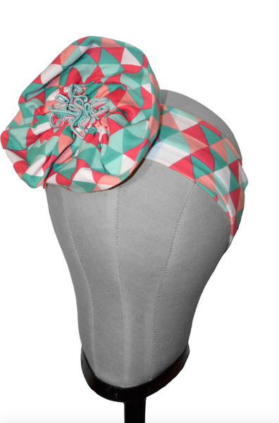 Triangle Aqua pre-tied turban headband displayed on a mannequin head featuring a geometric knit print and center flower detail.
