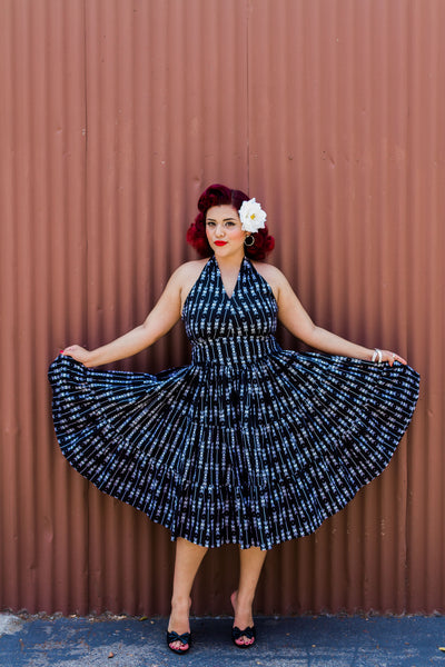 Model wearing the Wanda Dress in black arrow print, holding out the full tiered swing skirt to showcase the vintage silhouette.