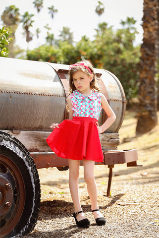 Girl wearing the Triangle Aqua Wendy Top with geometric print and Peter Pan collar paired with a red Kids Jivin' Skirt beside a vintage trailer.